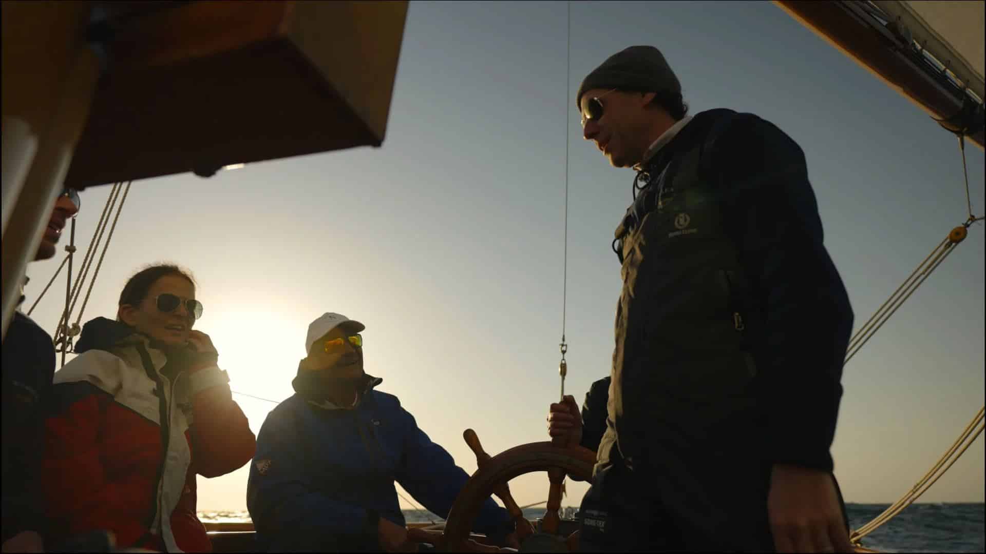 Invités et équipage à la barre à roue de Belle Aventure au coucher du soleil
