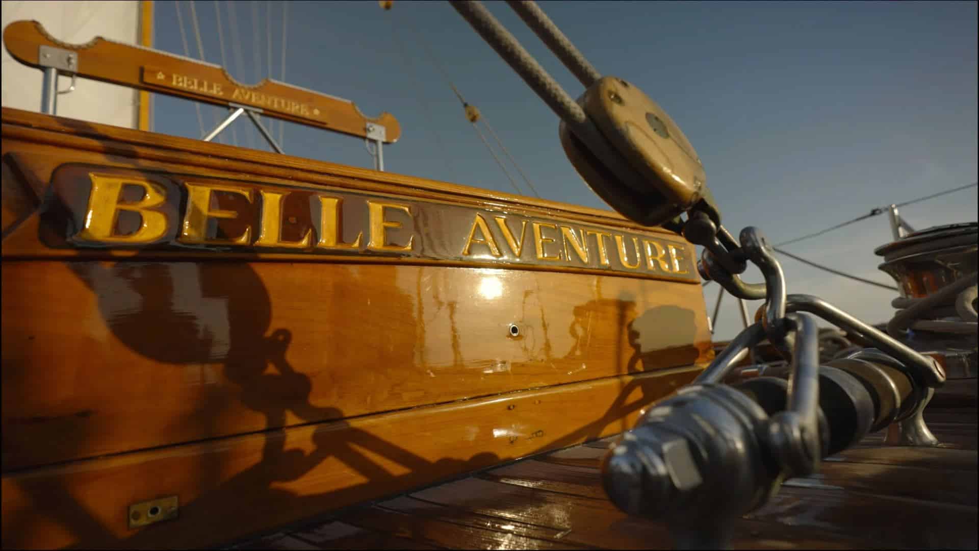 Nom Belle Aventure en lettres dorées sur le bois verni du voilier classique